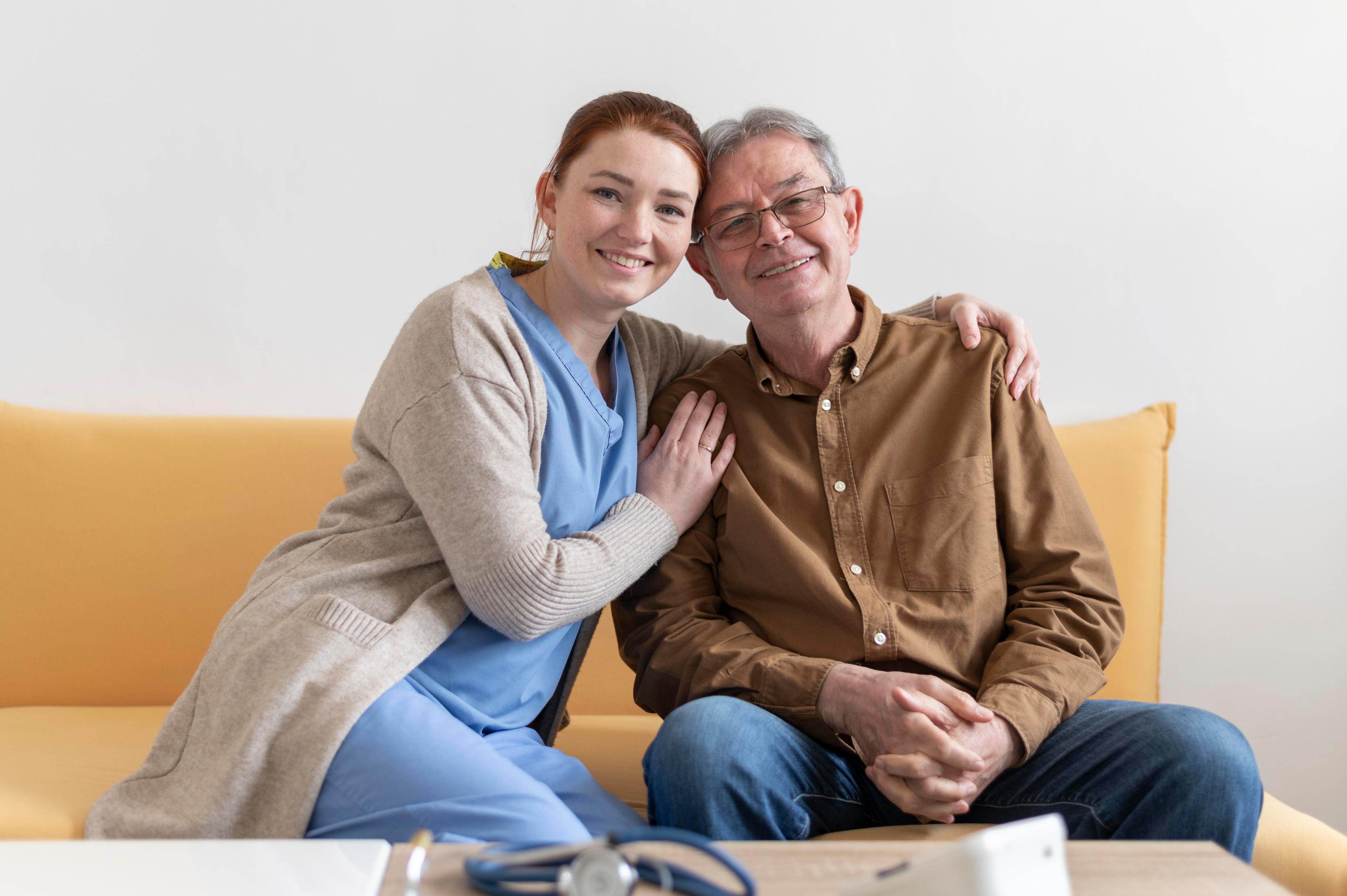 Caregiver hugging an elderly man while sitting on a couch.