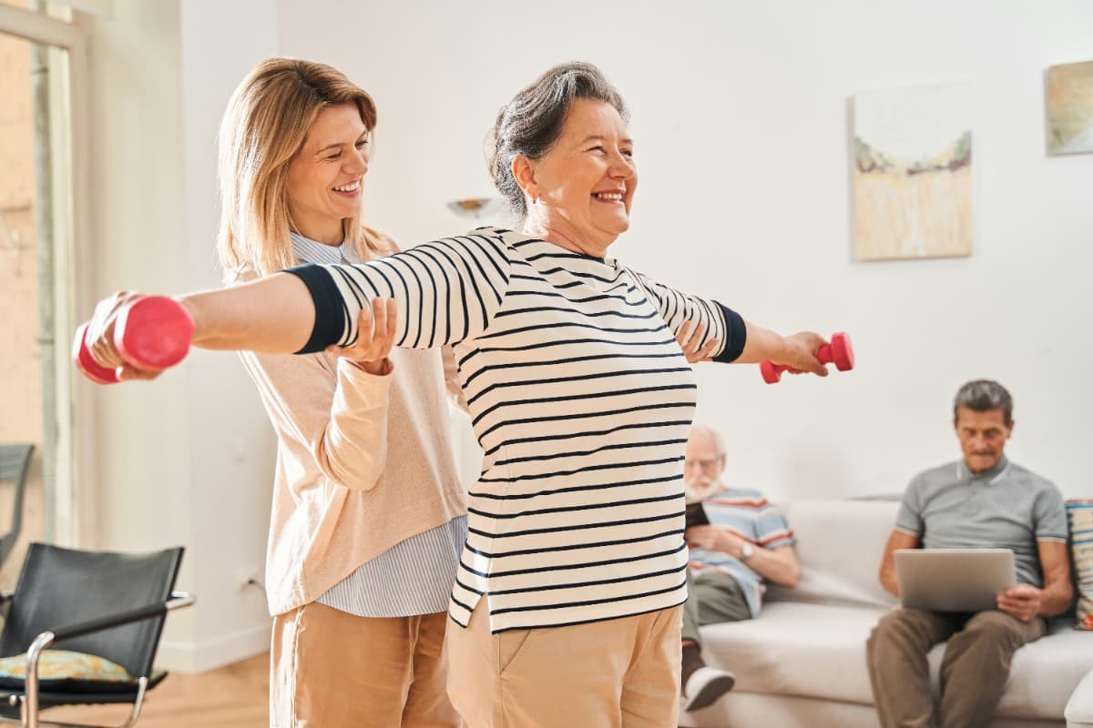 Caregiver helping an elderly woman exercise with dumbbells.