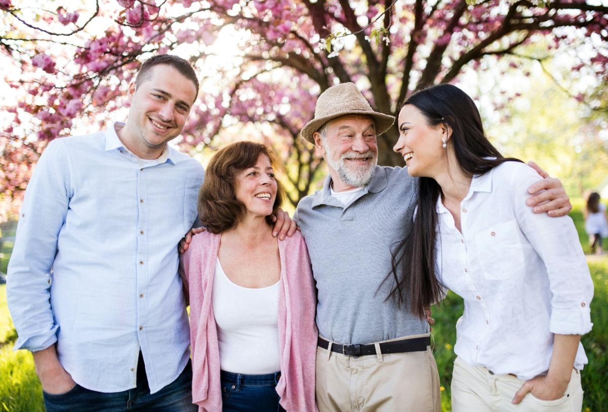 Smiling family of four standing outdoors under blooming trees.