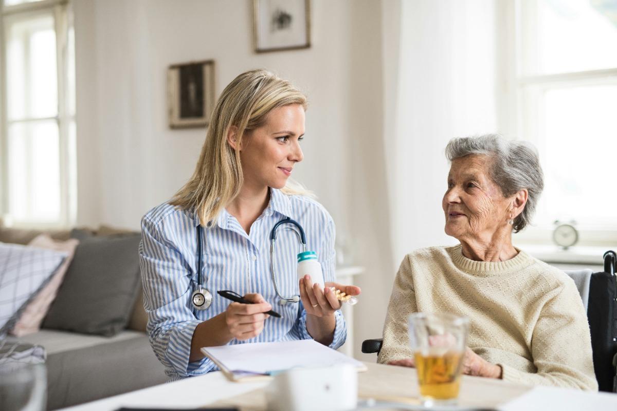 A healthcare worker holding medication talks to an elderly woman.