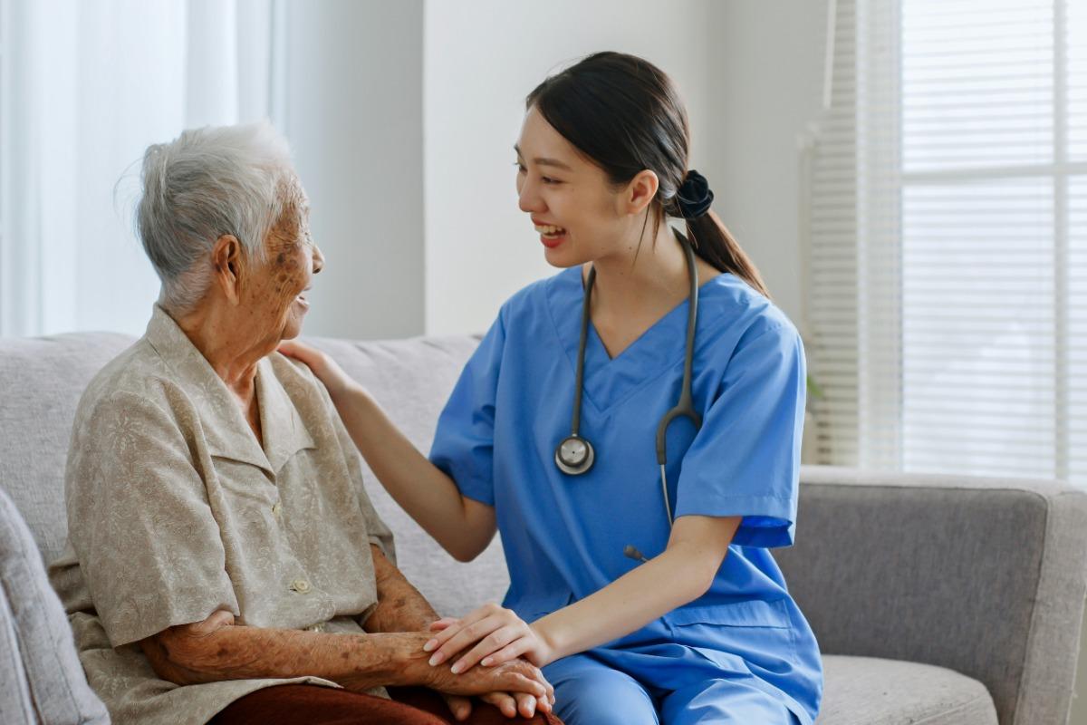 Nurse smiling and talking to an elderly woman on a couch.