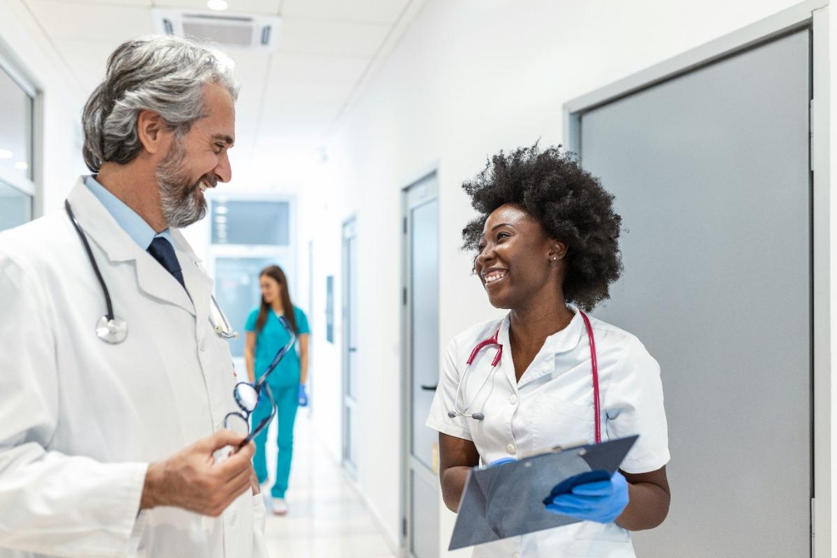 Doctor and nurse smiling and talking in a hospital hallway.