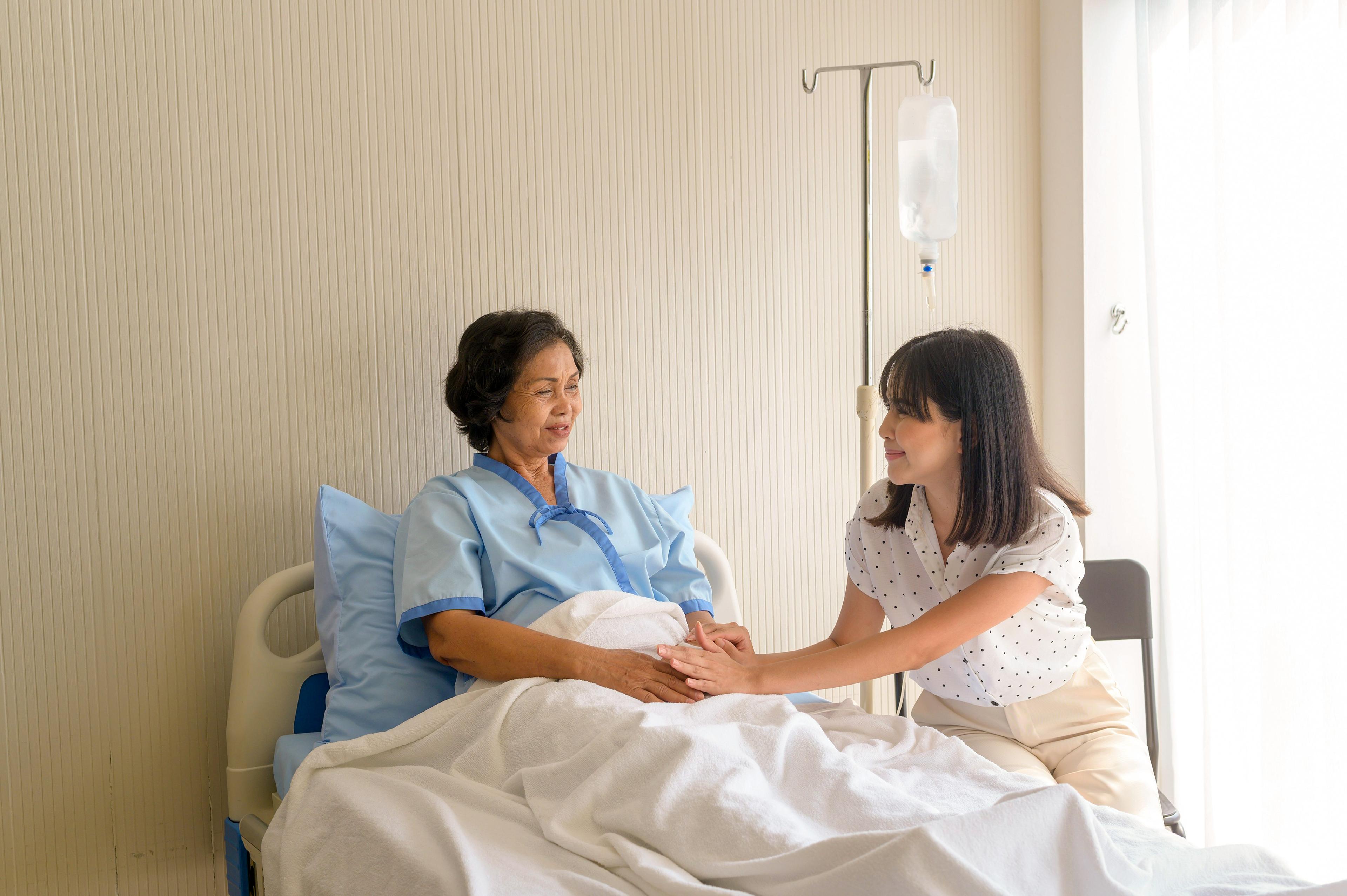 Caregiver comforting a patient in a hospital bed.