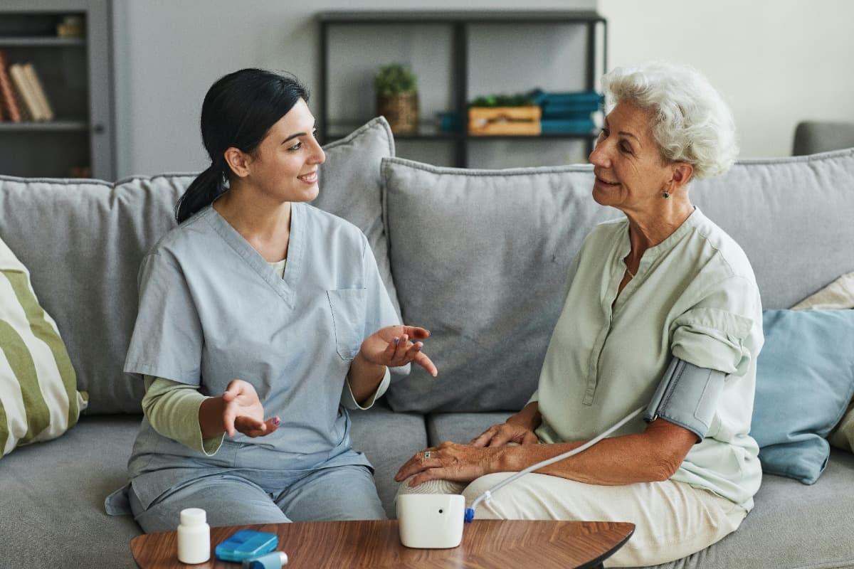 Caregiver talking to elderly woman with a blood pressure monitor.