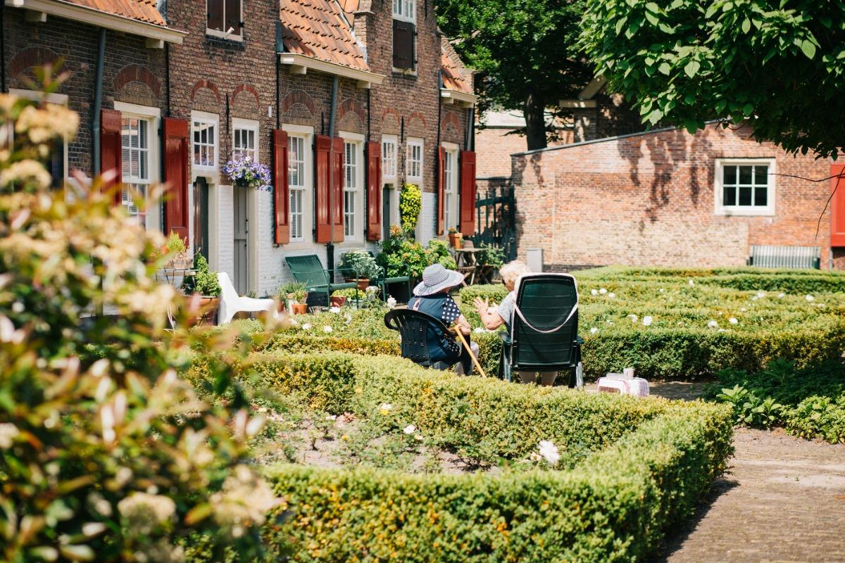 Elderly people sitting in a garden outside a long-term care facility.