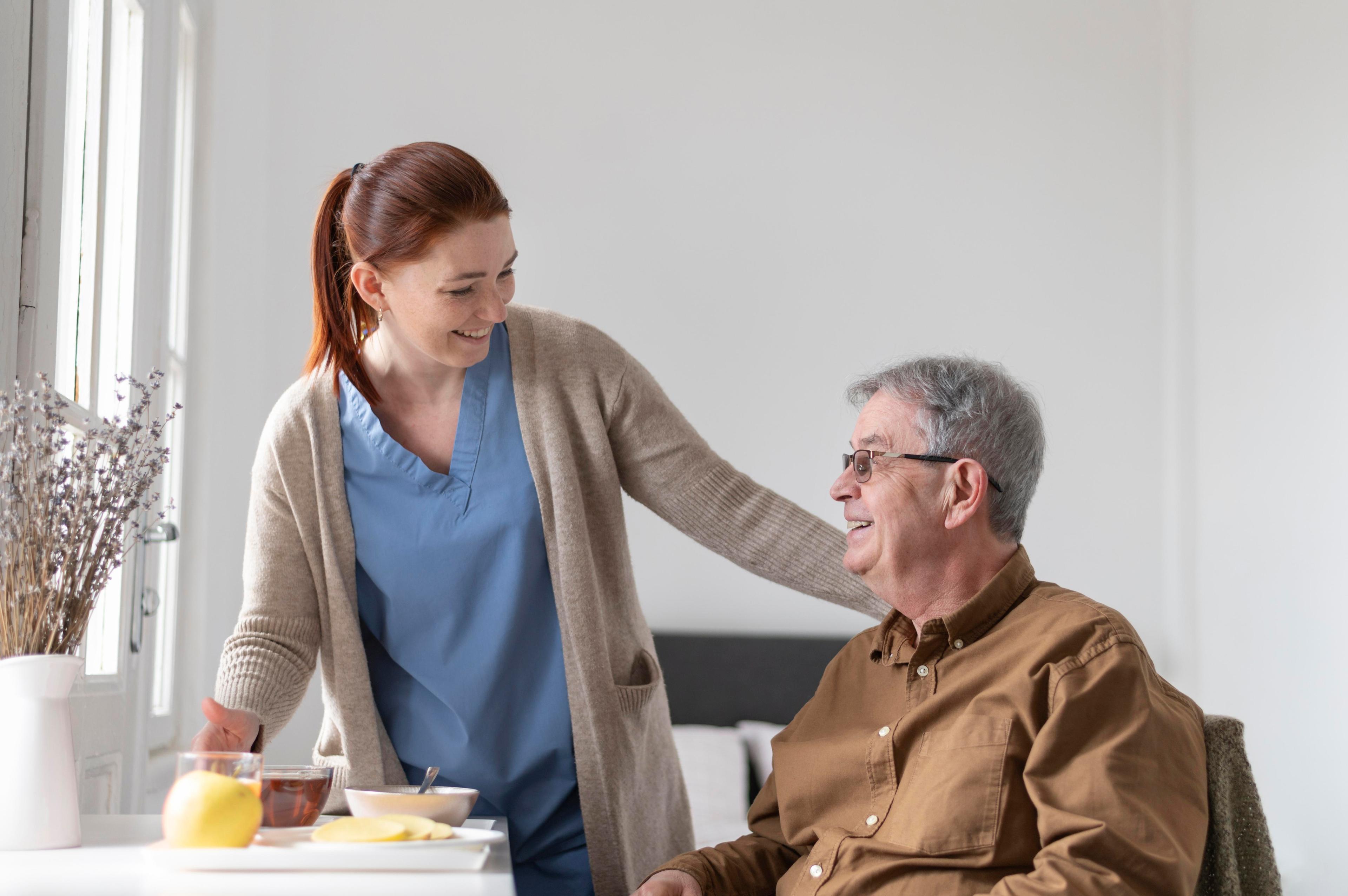 Caregiver smiling and talking to an elderly man at a table.