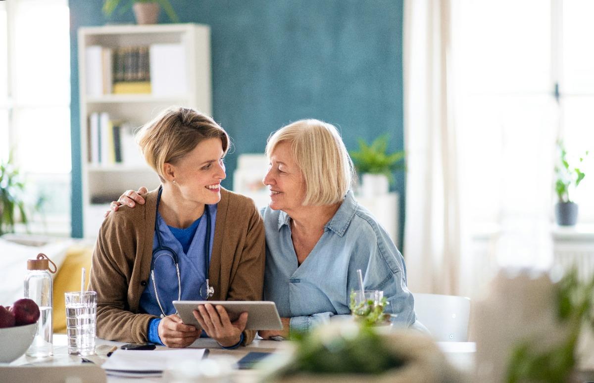 Caregiver with a tablet, smiling with an elderly woman.