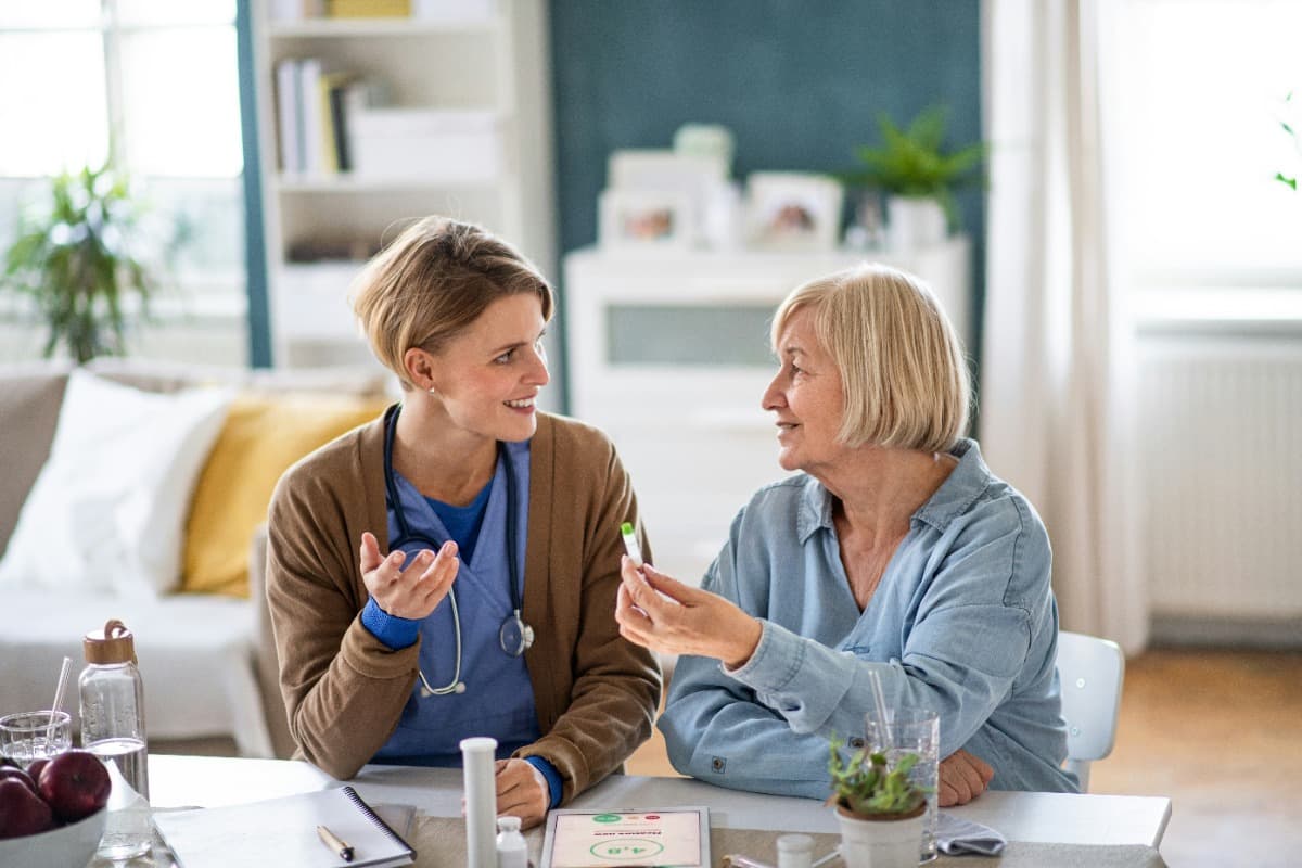 Caregiver discussing medication with an elderly woman at a table.