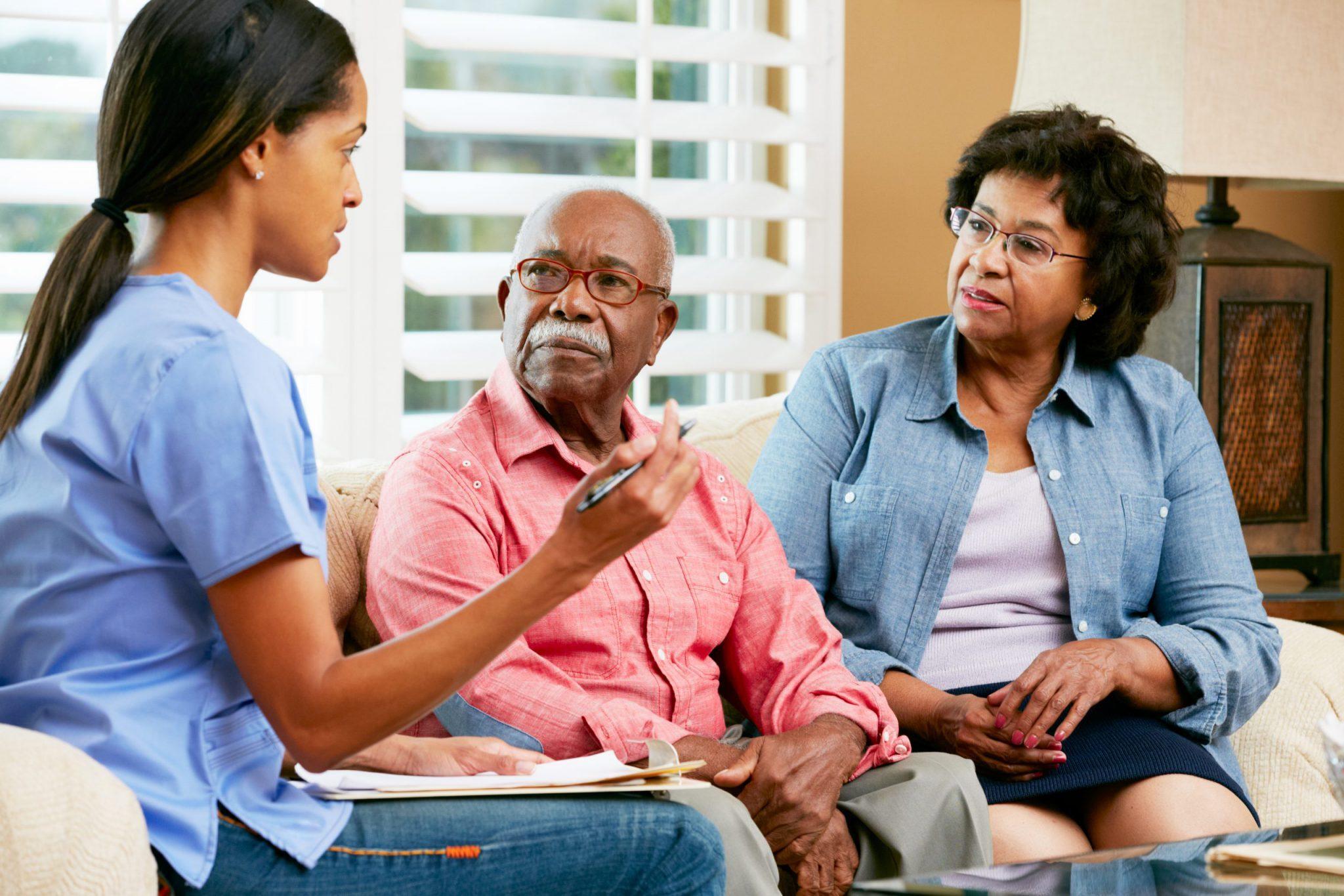 Nurse discussing with an elderly couple in a living room.