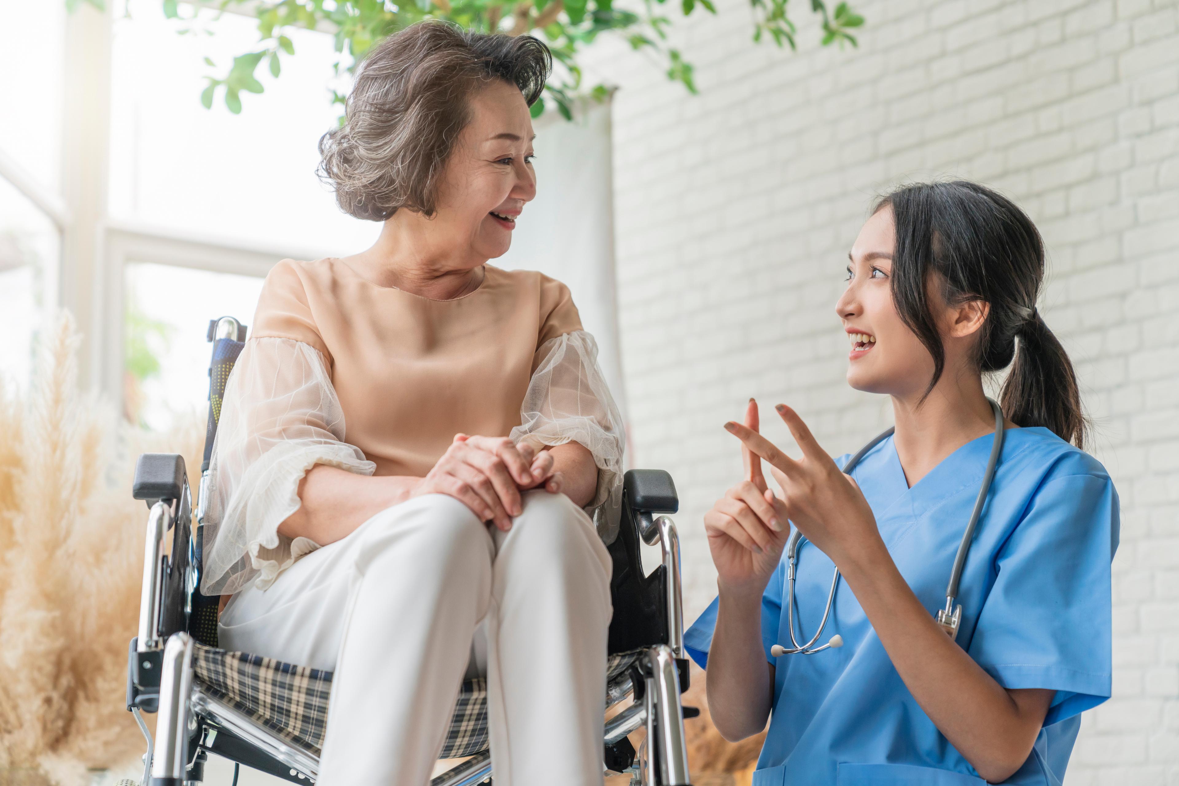 Nurse talking to a smiling elderly woman in a wheelchair.