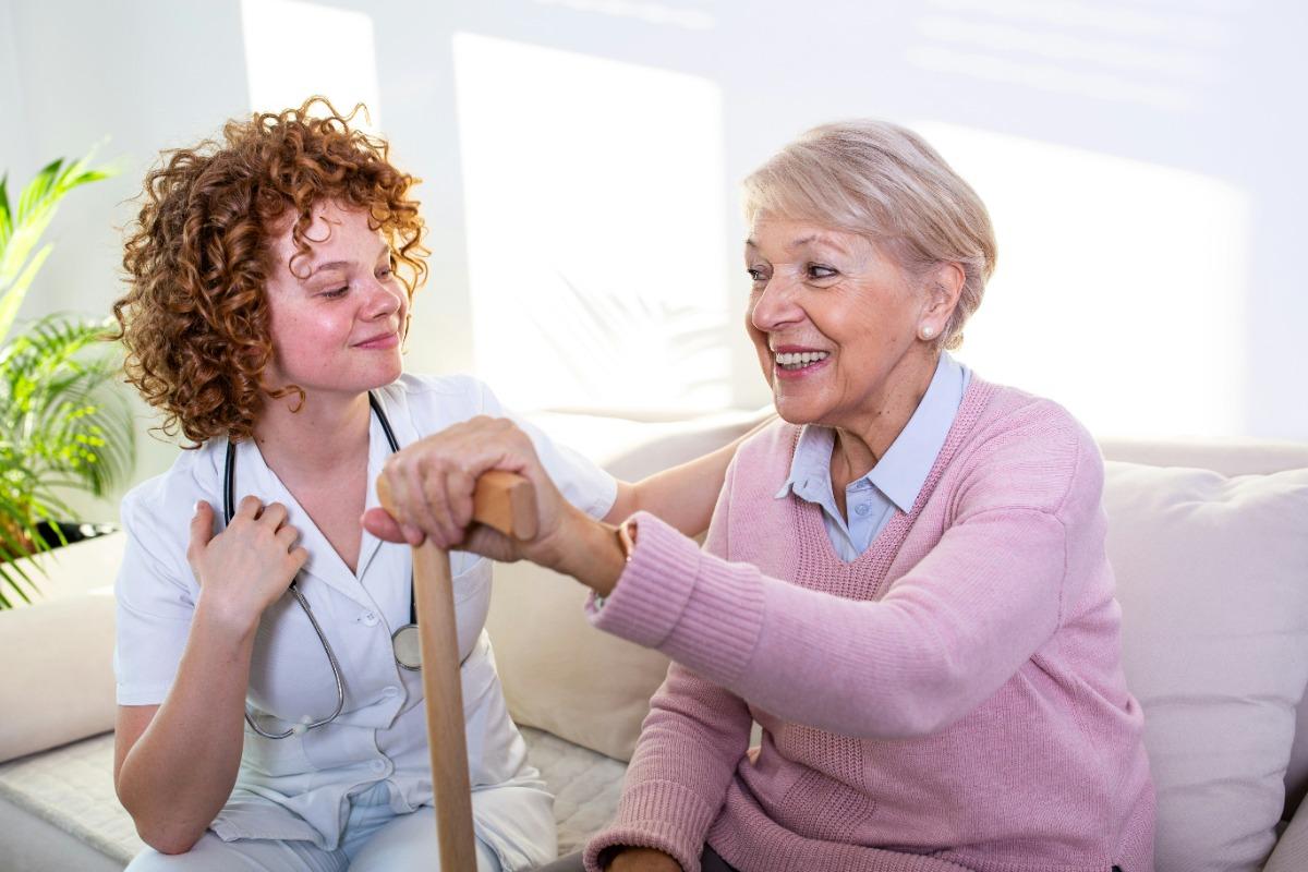 Therapist assisting a smiling elderly woman with a cane.