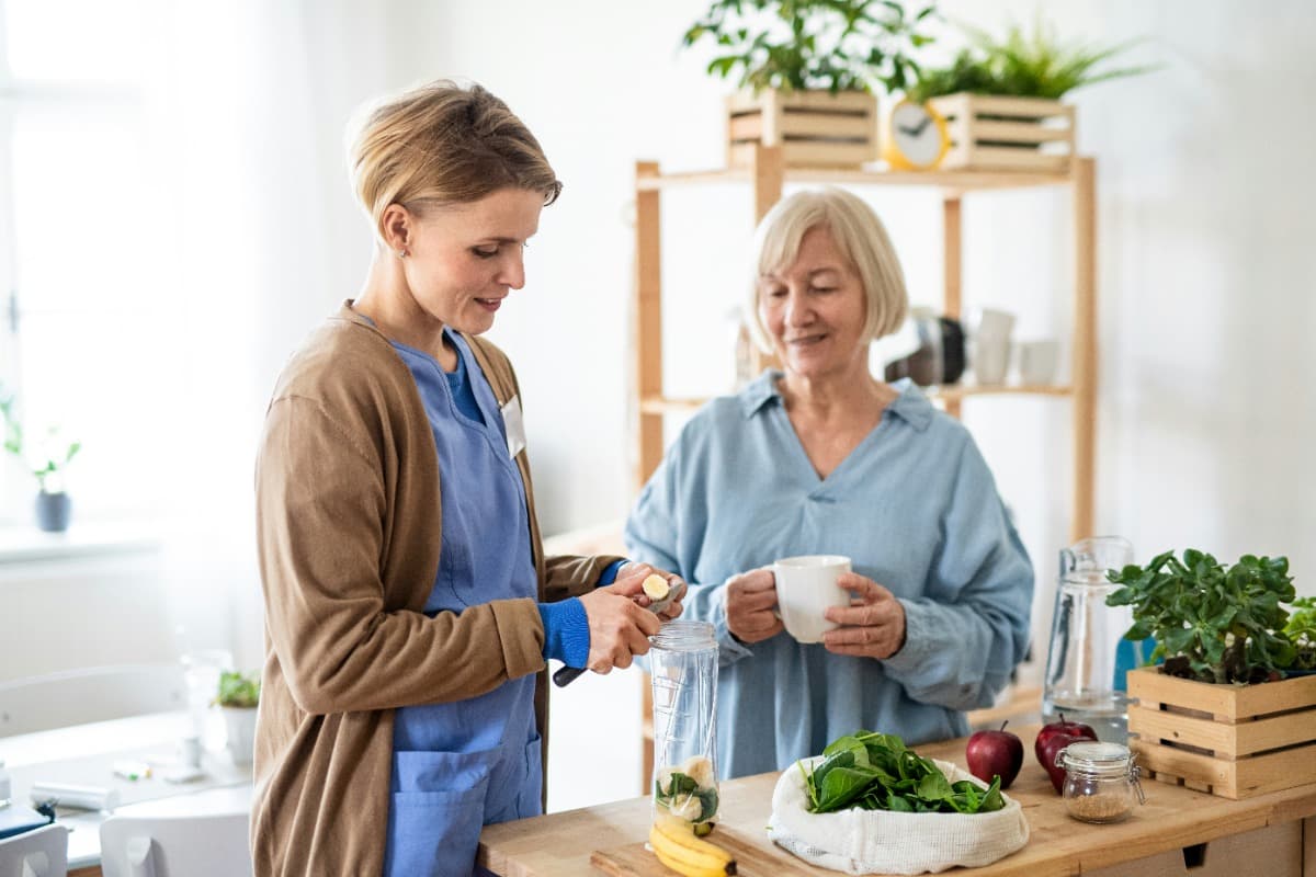 Caregiver preparing food with an elderly woman in a kitchen.