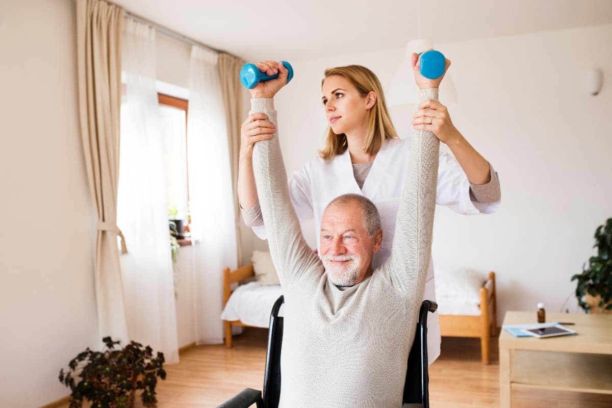 Therapist assisting an elderly man with arm exercises using dumbbells.