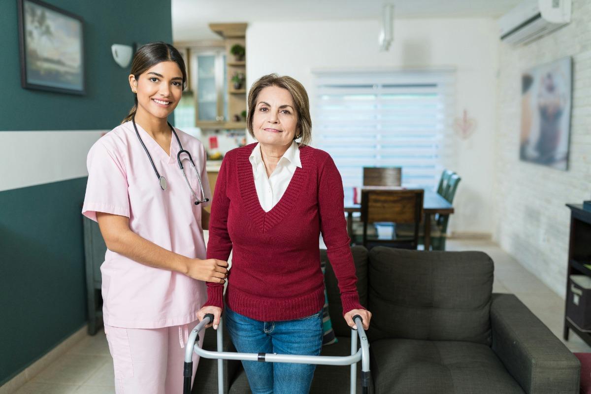 Caregiver assisting a woman with a walker in a living room.