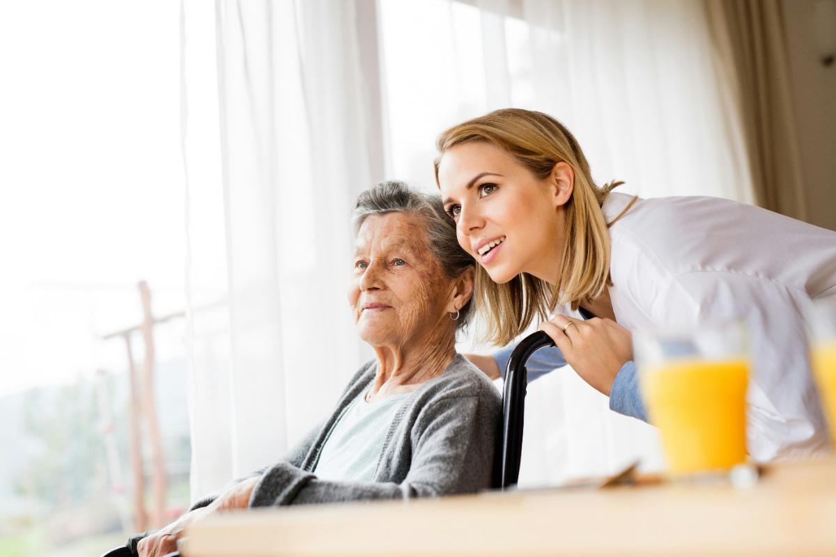 Caregiver leaning in to talk to an elderly woman in a wheelchair.