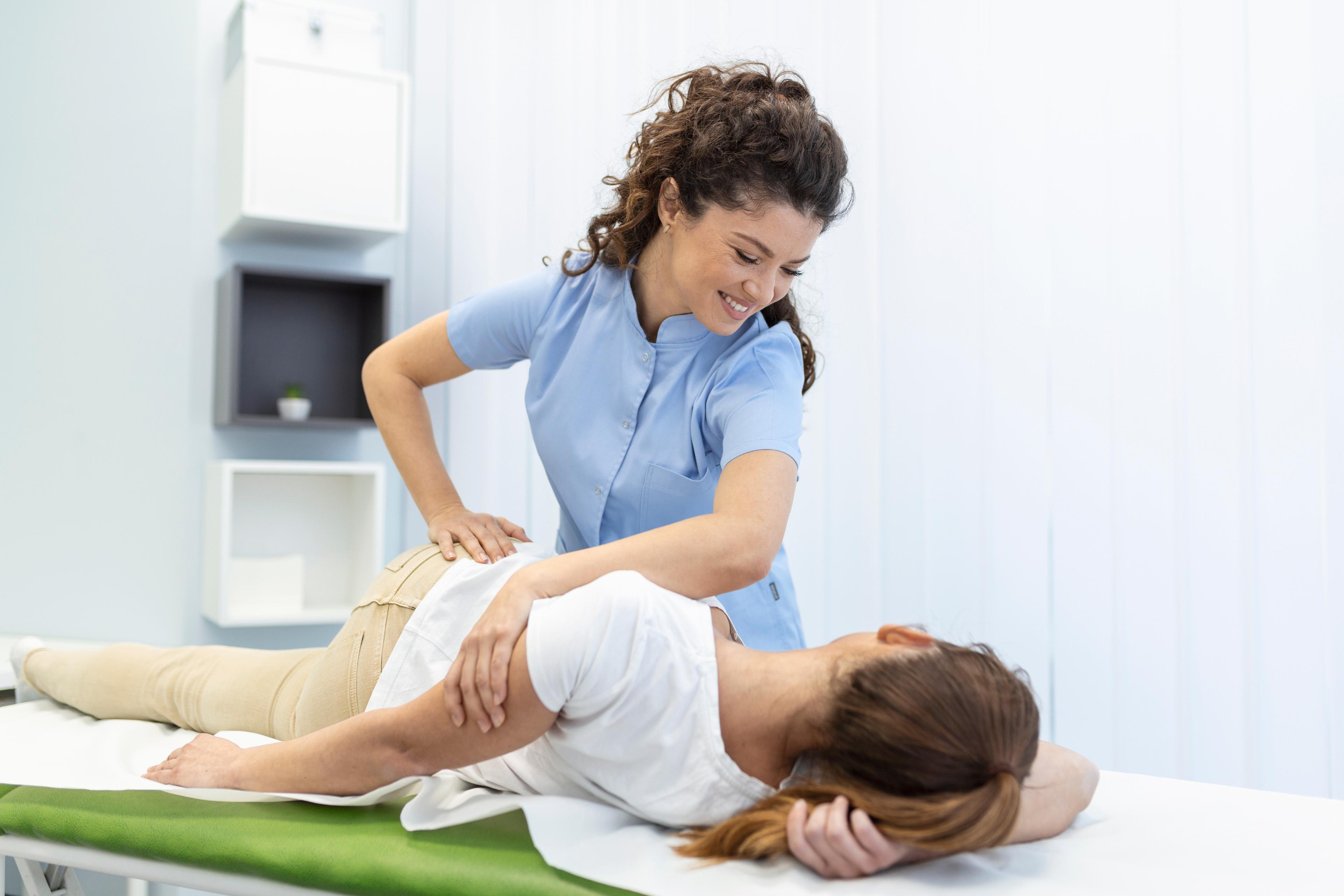 Therapist assisting a patient with a back stretch on a therapy table.