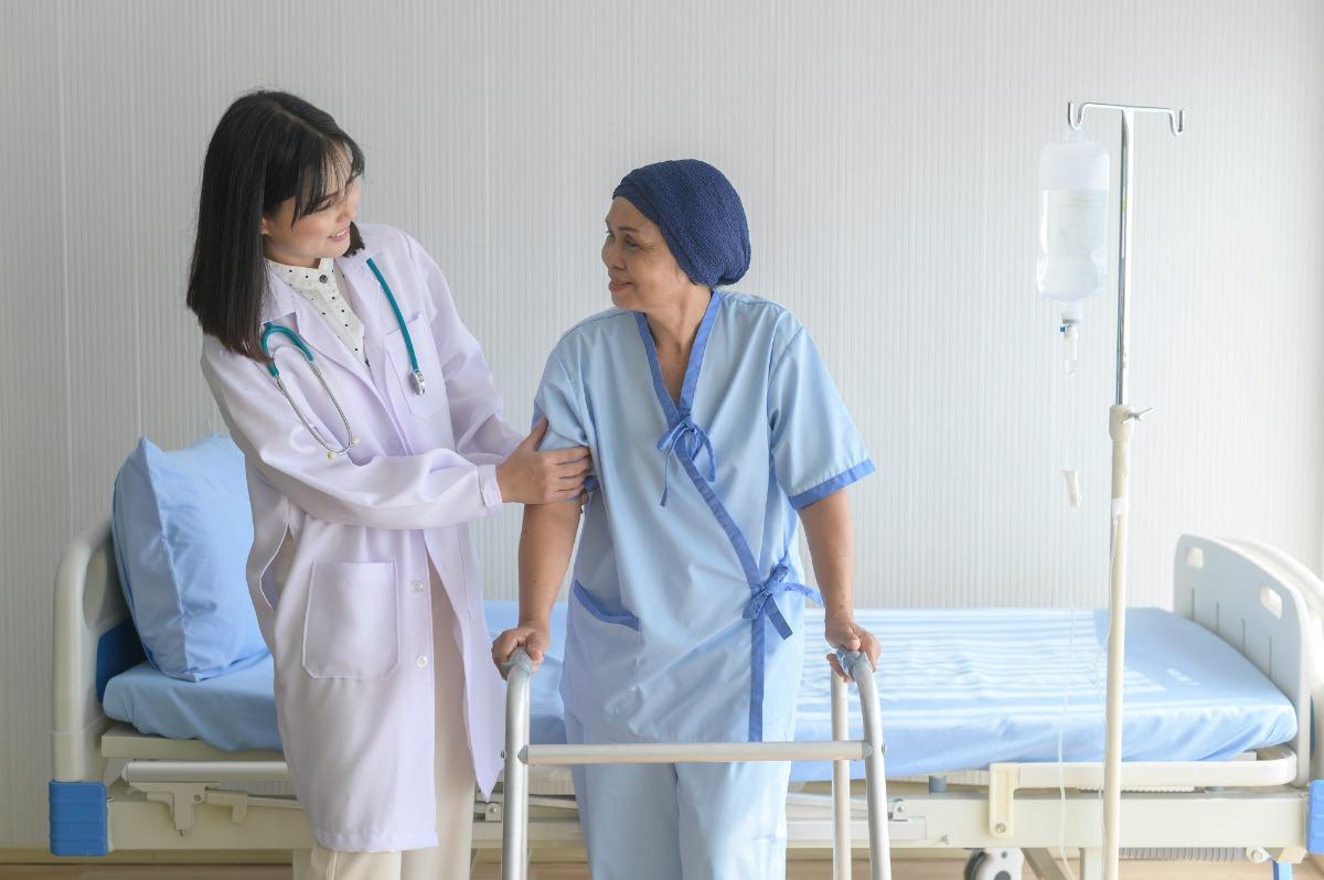 Nurse assisting a patient with a walker in a hospital room.