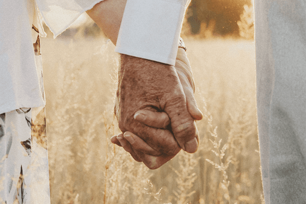 two seniors holding hands in a wheat field
